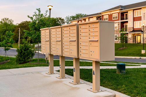 Cluster mailbox kiosk in a landscaped courtyard with an apartment building in the background at dusk
