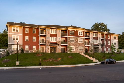 Apartment building elevation with landscaped mulch beds and a car parked out front at dusk