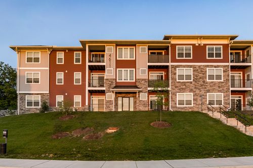 Apartment building corner with mixed-tone siding, an entry breezeway and fresh landscaping at dusk