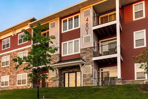 Close-up of an apartment building corner with a covered entry breezeway and a newly planted tree