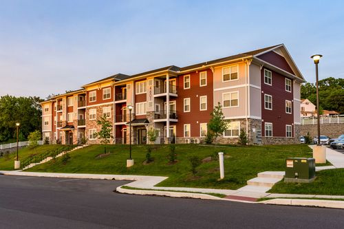 Apartment building elevation with red, tan and cream siding along a landscaped street at dusk
