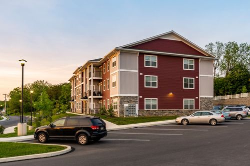 Apartment building corner with a curved driveway and cars parked beneath a darkening sky