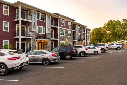 Apartment building entrance with a covered breezeway and a row of cars parked along a white fence