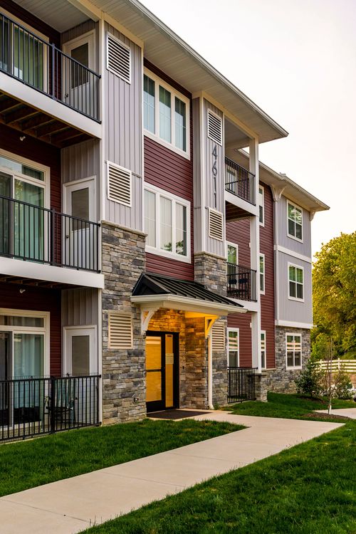Apartment building entry corner with a black canopy and a covered walkway toward a neighboring building