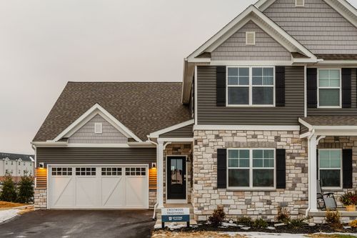 Two-story custom home exterior with gray siding, stone accents and a white carriage-style garage door in winter