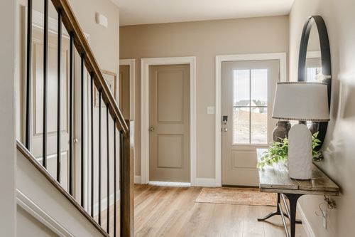 Hallway view past a paneled door toward a sunlit living room with wood flooring throughout