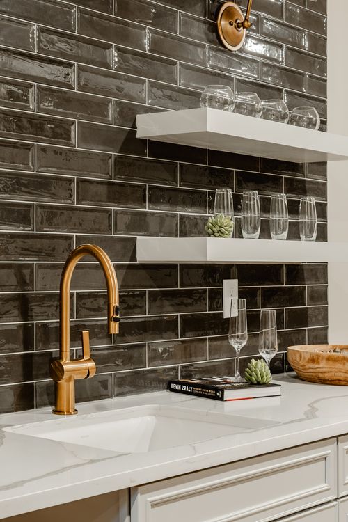 Wet bar corner with gold sconces, black tile and a framed print above the counter