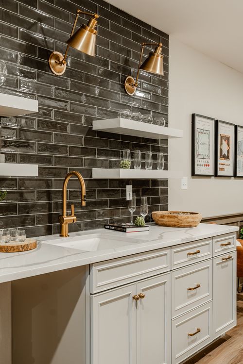 Basement wet bar with black tile, floating shelves and leather lounge chairs nearby