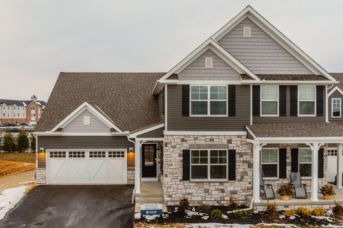 Close-up of a custom home entrance with stone veneer, black shutters and a white paneled garage door