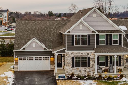 Two-story home exterior with stone base, dark shutters and a snow-covered lawn
