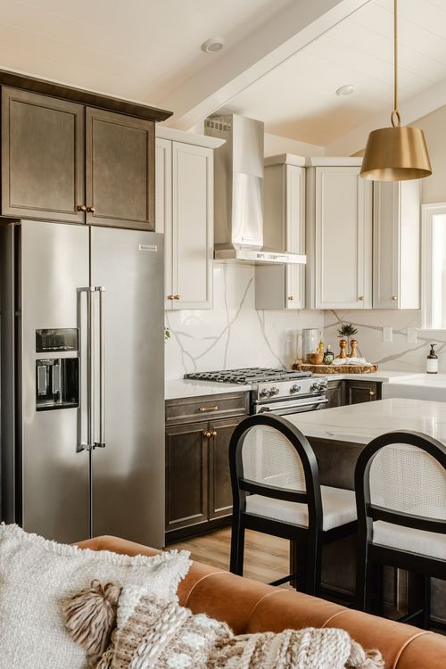 Kitchen with dark cabinetry, marble backsplash, gold pendant lights and a stainless range hood