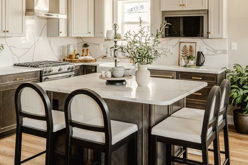 Kitchen with white cabinetry, stainless range and hood, and a veined marble backsplash