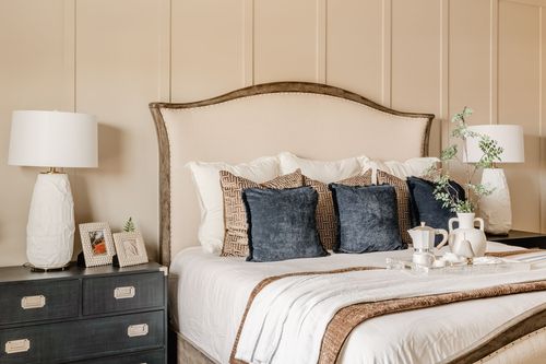 Bed with a tan upholstered headboard, navy velvet pillows and matching nightstand lamps