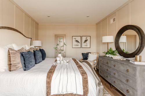 Bedroom with a round mirror over the dresser, navy pillows and bird artwork on the wall