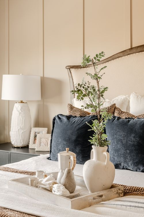 Close-up of a bed with navy pillows and a tray holding a teapot and vase