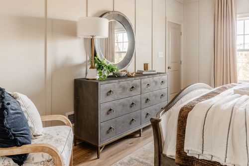 Dresser with a round mirror and white lamp beside an upholstered accent chair