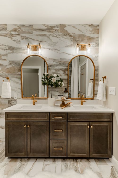 Wide view of a double vanity bathroom with marble tile and dark wood cabinetry