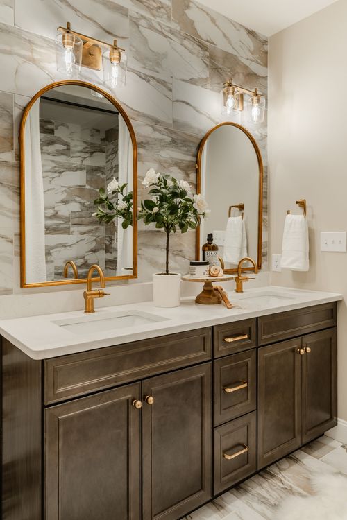 Double-sink vanity with marble tile, arched brass mirrors and a potted plant between the sinks