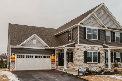 Aerial view of a custom home with tan siding, stone accents and a wide driveway in early spring