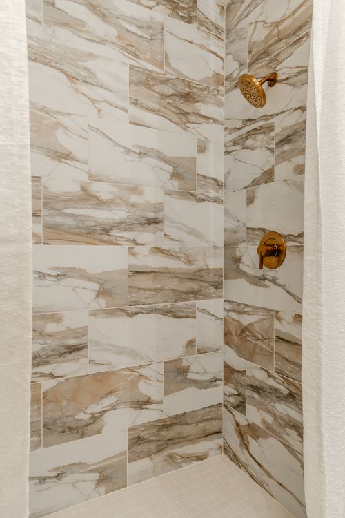 Walk-in shower with marble-look tile and a brass shower head and handle