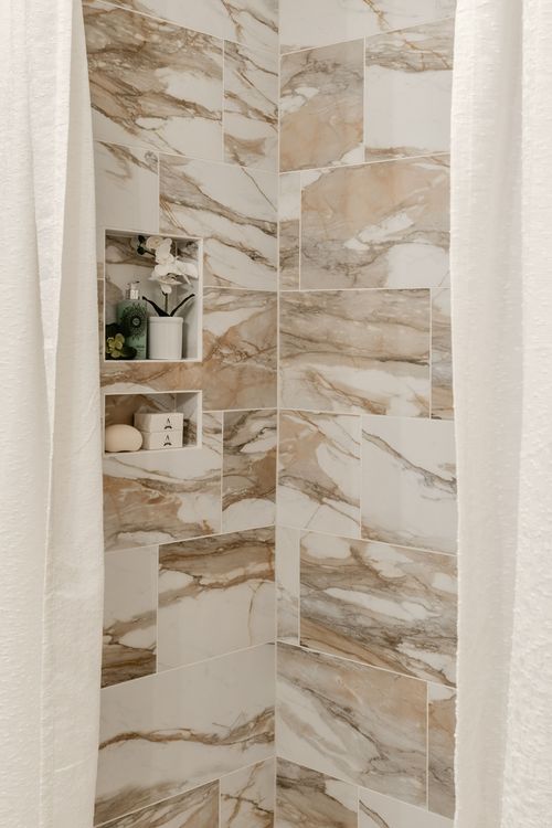 Walk-in shower with marble tile and a built-in niche holding toiletries
