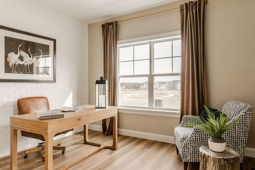 Home office with a leather chair, wood desk and framed bird print on a white brick accent wall
