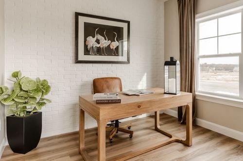 Home office desk with a leather chair and lantern-style candle holder against a brick accent wall