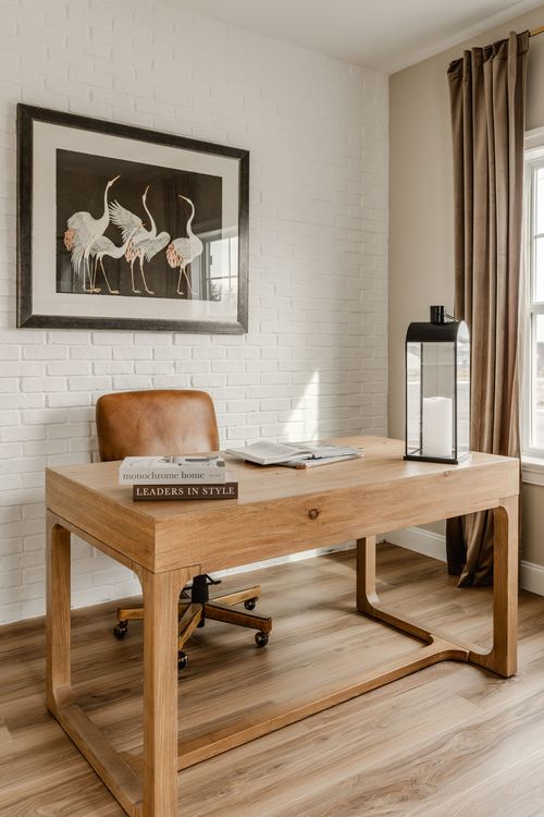 Home office with a wood desk, stacked books and crane artwork on a white brick wall