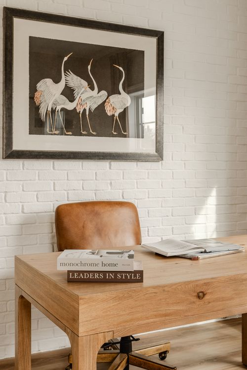 Home office desk styled with books, a lantern and framed crane artwork above