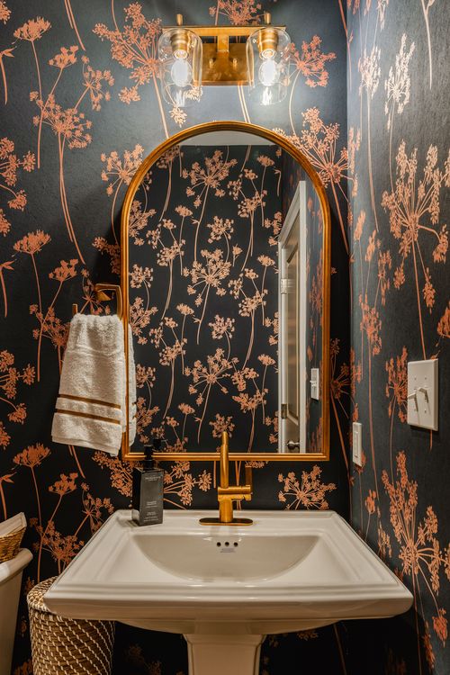 Close-up of a powder room pedestal sink with brass fixtures and floral wallpaper