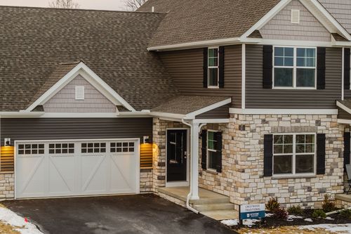 Wide aerial view of a custom home and driveway set among a new residential neighborhood