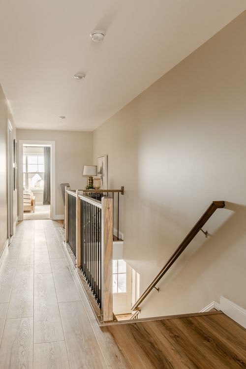 Upstairs hallway with a wood railing overlook and framed artwork along the wall