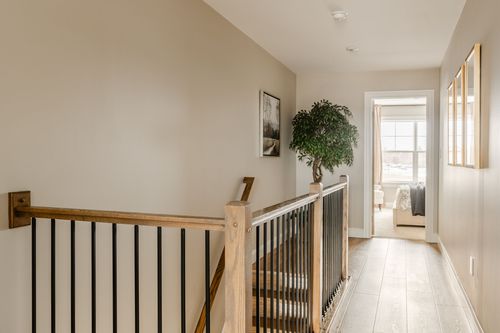 Upstairs landing with a wood railing, potted plant and view into a sunlit bedroom