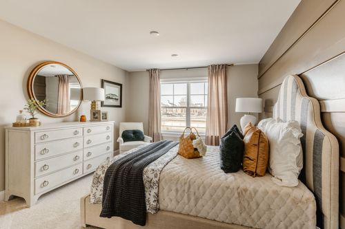 Bedroom with a round mirror over the dresser and warm-toned patterned bedding