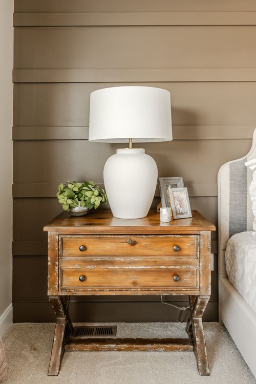 Distressed wood nightstand with a white lamp and framed photos beside the bed