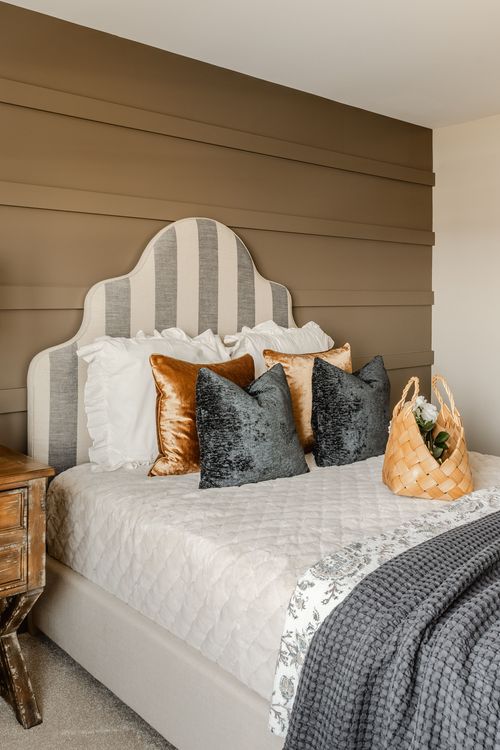 Bedroom with a striped headboard, rust and gray pillows and a woven basket bag on the bed