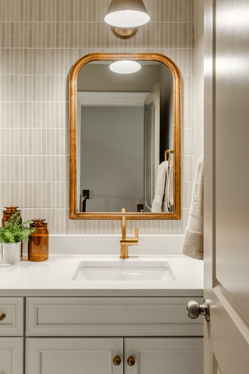 Close-up bathroom vanity with an arched gold mirror, gold faucet and vertical tile backsplash