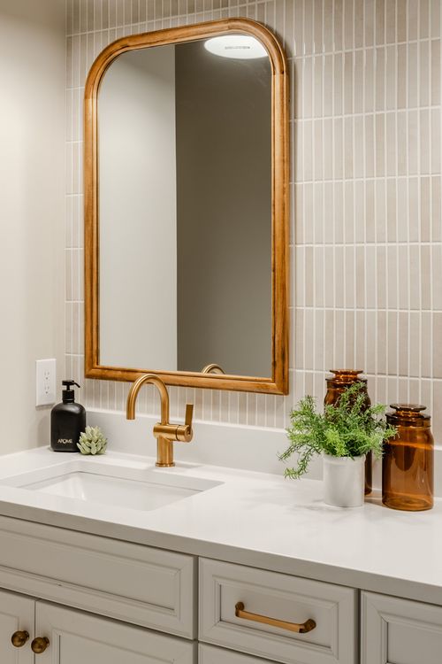 Bathroom vanity with a gold arched mirror, gold faucet and gray cabinetry