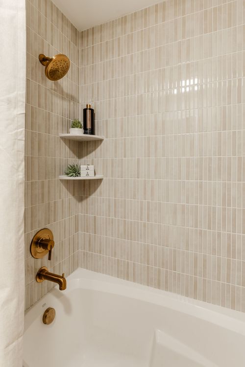 Tub and shower with vertical tile, a brass shower head and built-in corner shelves