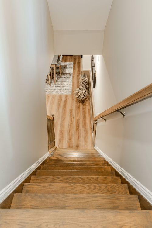 Staircase leading down to a lower-level living space with a wood floor and woven pendant lanterns