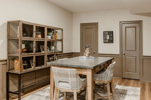 Basement flex room with a glass display cabinet, wainscoting and a round table with wicker chairs