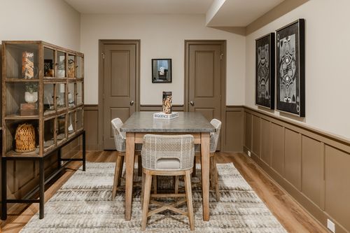Basement dining nook with wainscoted walls, framed artwork and a round table set for guests
