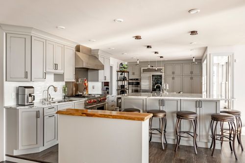 Light gray kitchen with a wood live-edge bar top, stainless range hood and upholstered bar stools