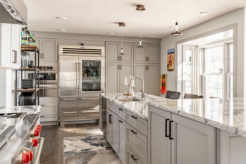 Kitchen wide view with gray cabinetry, marble island and bay window seating area
