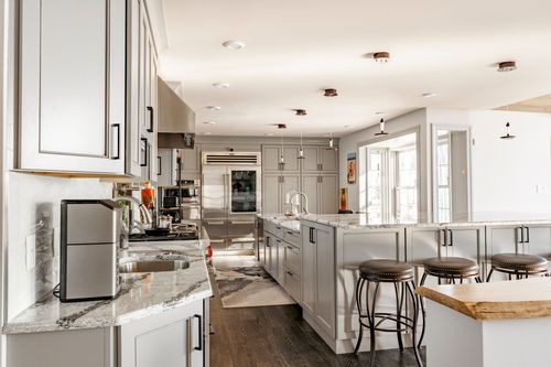 Kitchen with open metal shelving, gray cabinetry, marble island and bar stools