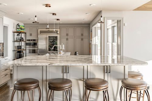 Kitchen island with marble waterfall counter, copper pendant lights and leather bar stools