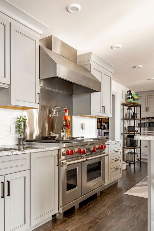 Stainless steel range hood over a red-knobbed gas range with pot filler faucet