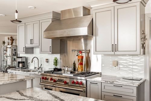 Gray kitchen cabinetry with stainless range hood, red-knobbed range and pendant lights