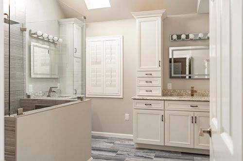 Primary bathroom with vaulted skylight, glass shower stall and floating white vanity towers
