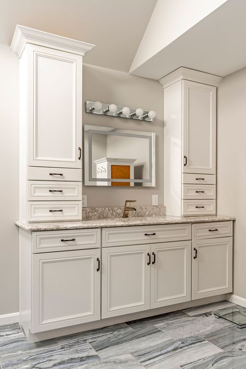 Bathroom vanity with white linen towers, granite counter and lit mirror